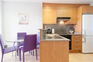 eine Küche mit lila Stühlen, einem Tisch und einem Kühlschrank in der Unterkunft Global Properties, Apartamento con terraza y piscina en la playa de Canet in Canet d'en Berenguer