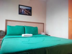 Una cama con colcha verde y una toalla blanca. en Easton Park Residence Jatinangor - GIANDARA, en Sayang