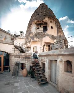 uma mulher de pé nas escadas de um velho edifício em Kelebek Special Cave Hotel & Spa em Goreme