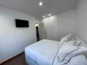 a white bedroom with a bed and a tv on a wall at Chalet exclusivo bonalba in Alicante