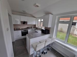 a kitchen with white cabinets and a counter with stools at A Beautiful Premium 4-Bedroom House With Parking (Reading West) in Reading
