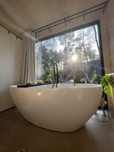 a large white bath tub in a room with a window at Vague Luxurious Tiny House Luxe Wellness, Spa Bad,Beamer, Veluwe in Nunspeet
