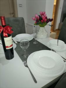 uma mesa com pratos brancos e uma garrafa de vinho e flores em Apartman Mima em Sombor