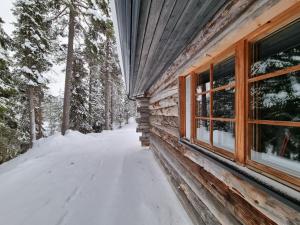 ein Blockhaus im Schnee neben einem Fenster in der Unterkunft Salmenkelo in Kuusamo