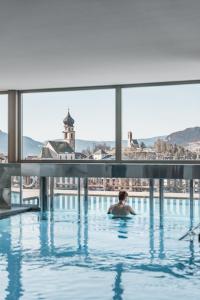 Ein Mann im Pool mit Blick auf die Stadt. in der Unterkunft Hotel Emmy - five elements in Völs am Schlern