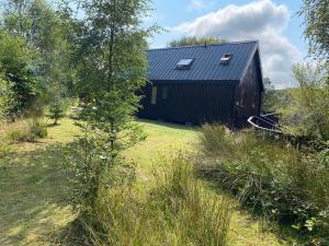 eine schwarze Scheune mit einem Sonnendach auf einem Feld in der Unterkunft Loch Aweside Forest Cabins in Dalavich