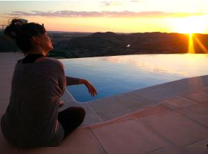 una mujer sentada en el borde de una piscina viendo la puesta de sol en Casas Rurales Planeta Chicote, en Zafra de Záncara