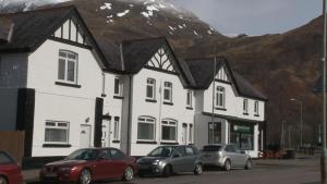 un bâtiment avec des voitures garées devant lui et une montagne dans l'établissement Highland Getaway, à Kinlochleven