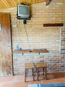 een tv zittend op een stenen muur met twee krukken bij Chalé buraco do tatu in Conceição da Ibitipoca