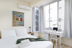a white bedroom with a bed and a desk and window at Gordon Seaside 4BDR apt in TLV in Tel Aviv