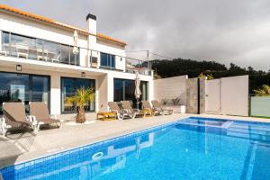 a swimming pool with chairs and a house at Casa Bella Vista - Calheta in Arco da Calheta