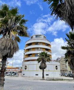 een wit gebouw met palmbomen ervoor bij Cosy Sea View Apartment in Costa da Caparica