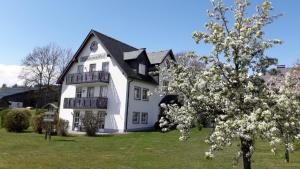 a white house with a black roof and a flowering tree at Gästehaus Frankenwaldhof in Bad Steben
