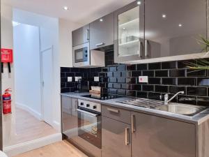 a kitchen with stainless steel appliances and black tiles at Designer Flat with Parking near Peckham & Brixton in London