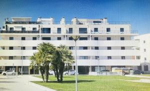 a large white building with palm trees in front of it at Condomínio Ondas do Mar -Coastal Comfort- in Olhão