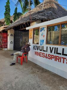 a man sitting on a red chair in front of a building at 2 Bed House - Sleeps 3 - Pool - Parking - Wifi in Ukunda +3 photos
