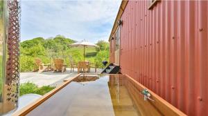 a red house with a pool and a table and an umbrella at Beech Shepherds Hut in Dittisham