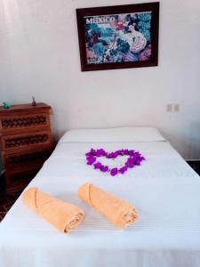 Una cama con dos toallas y flores moradas. en La lagartija, en San Pablo Etla