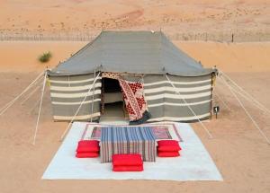 a tent in the middle of a desert with red chairs at Desert Wonders Camp in Ḩawīyah
