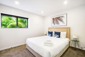 a white bedroom with a large bed and a window at Forest View Apartment with Parking and Garden in Auckland