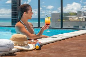 uma mulher sentada ao lado de uma piscina segurando uma bebida em Palms Ponta Verde by Tropicalis em Maceió