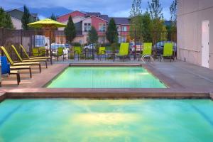 a swimming pool with chairs and a table and an umbrella at SpringHill Suites by Marriott Salt Lake City-South Jordan in South Jordan