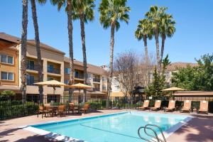 una piscina con sillas, mesas y palmeras en Courtyard Milpitas Silicon Valley en Milpitas