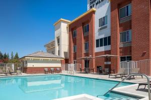 a swimming pool in front of a building with tables and chairs at Fairfield Inn & Suites by Marriott Visalia Tulare in Tulare