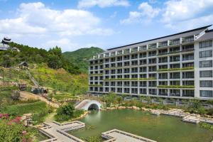a building with a pond in front of a mountain at Sheraton Maoming Hot Spring Resort in Maoming