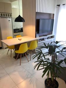a dining room table with yellow chairs and a tv at Apartamento próximo ao Beto Carrero. in Penha