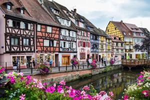 a group of buildings next to a river with flowers at Studio Le Belvédère TURCKHEIM in Turckheim