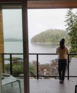 a woman standing on a balcony looking out at the water at Duffin Cove Resort in Tofino