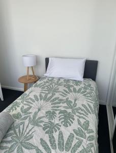 a bed with a green and white blanket and a lamp at Eloura Gardens 100m to Beach in Cronulla