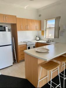 a kitchen with a white refrigerator and wooden cabinets at Eloura Gardens 100m to Beach in Cronulla