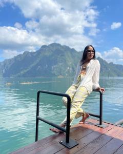 a woman sitting on a rail on a dock near the water at Panvaree Resort in Ratchaprapha