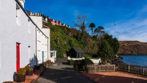 a white house with a red door next to the water at Harbour House in Portree