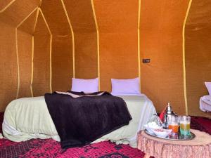 a bed in a tent with a table next to it at Merzouga Desert Campsite &Activities in Merzouga