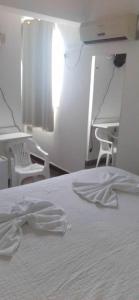 a bedroom with a white bed with chairs and a desk at Hotel Aurora in Alagoinhas