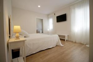 a white bedroom with a bed and a table with a lamp at Casa Verata in Losar de la Vera