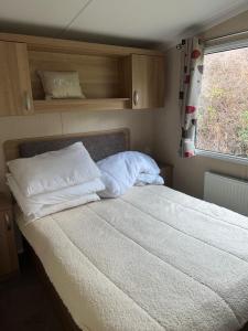 a bedroom with a bed with white pillows and a window at 3 Bed Platinum Caravan PRESTHAVEN SANDS in Prestatyn +7 photos