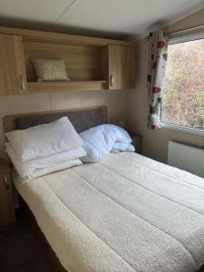 a bedroom with a bed with white pillows and a window at 3 Bed Platinum Caravan PRESTHAVEN SANDS in Prestatyn