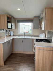 a kitchen with white cabinets and a sink and a window at 3 Bed Platinum Caravan PRESTHAVEN SANDS in Prestatyn