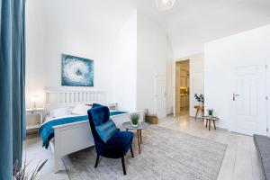 a white bedroom with a bed and a blue chair at Mlynska Center Apartment Kosice with private Parking in Košice