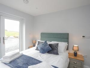 Cama blanca con almohadas azules y ventana en Tan Y Coed - Nasareth en Caernarfon