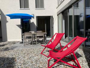 2 sillas rojas y una sombrilla en el patio en MarAvilia Apartment, vicino al Monte Tamaro e al parco acquatico Splash & SPA, en Monte Ceneri