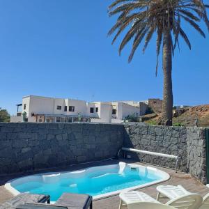 a swimming pool with chairs and a palm tree at Casona La Orilla 1908 Tías in Tías