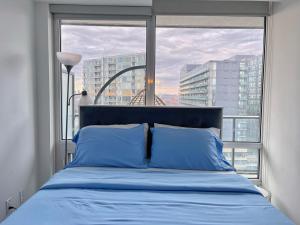 łóżko z niebieskimi poduszkami w pokoju z oknem w obiekcie Exquisite Condo By Exhibition Place Downtown Toronto w mieście Toronto