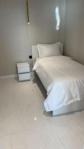 a white bedroom with a bed and a night stand at Damac Al Jawharah Tower Apartments in Jeddah