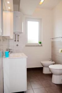 La salle de bains blanche est pourvue de toilettes et d'une fenêtre. dans l'établissement Apartman Maria 1, à Rab