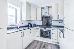 a white kitchen with white cabinets and a sink at 2 Bedroom City Centre Apartment in High Wycombe with Parking in High Wycombe